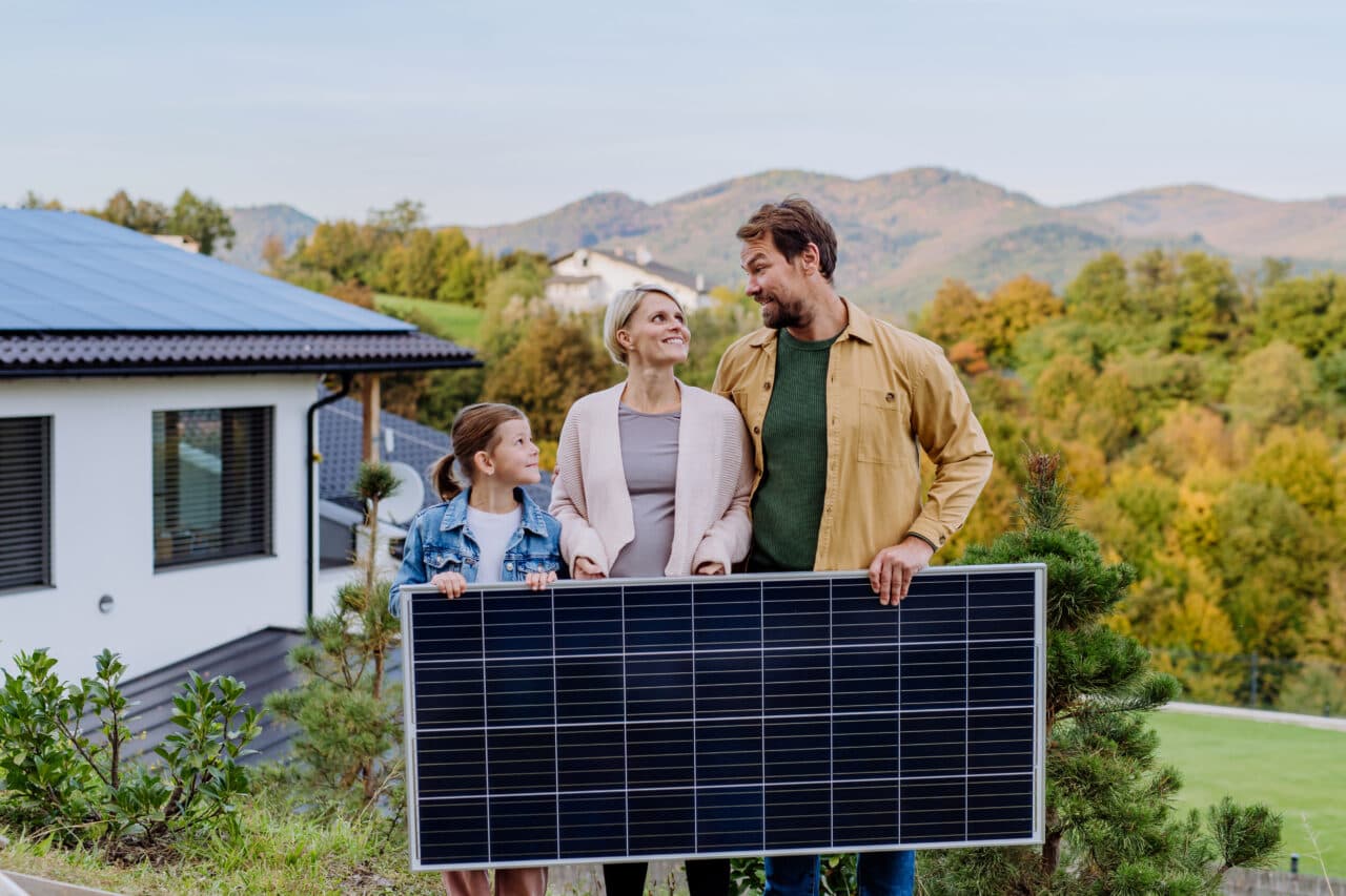 Glad familie med solcellepanel foran huset